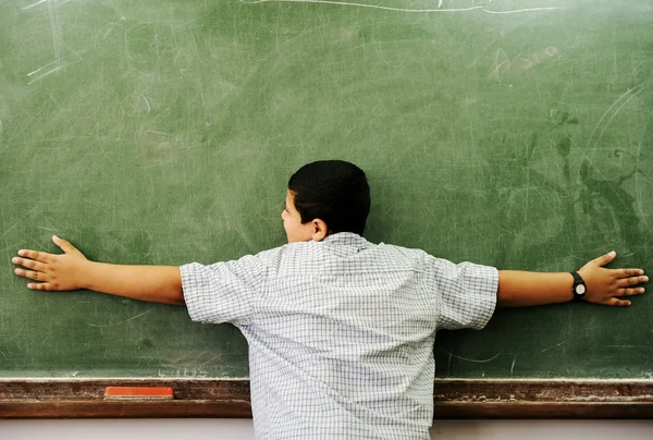 Schoolchild hugging board in classroom — Stock Photo, Image