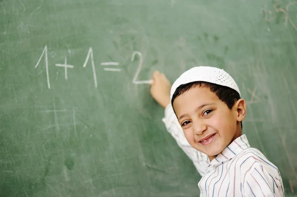 Niño muy lindo y positivo sonriendo y escribiendo en el tablero de la escuela — Foto de Stock
