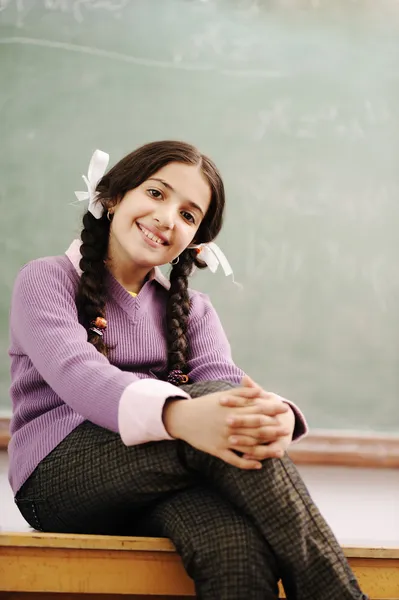 Симпатичная школьница сидит на столе в классе — стоковое фото