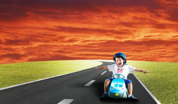 Happy kid on green meadow driving a car — Stock Photo, Image
