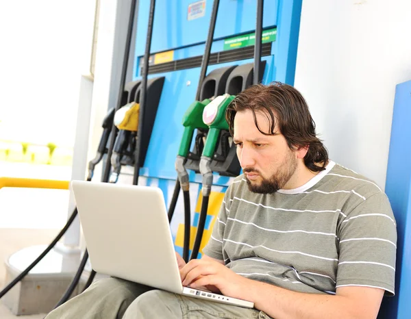 Ένας άνθρωπος με ανησυχούν πρόσωπο με φορητό υπολογιστή σε σταθμό καυσίμων — Φωτογραφία Αρχείου