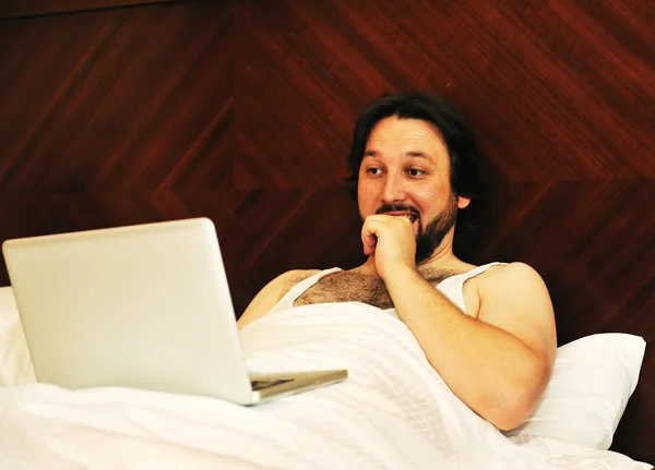 Чоловік на ноутбуці в спальні дивиться на щось — стокове фото