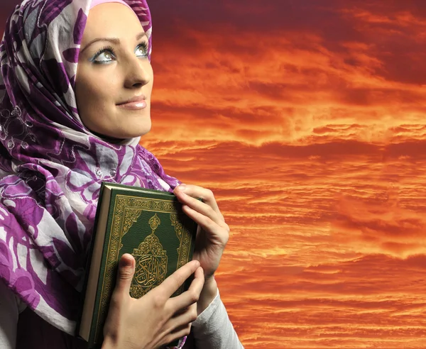 Adorable chica musulmana sosteniendo el libro sagrado Corán, contra el cielo rojo —  Fotos de Stock