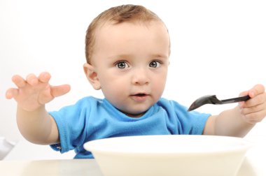 Cute adorable one year old baby with green eyes eating on table, spoon and clipart