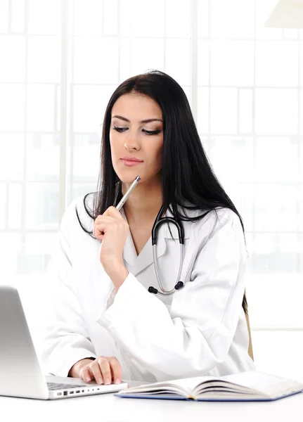 Młoda kobieta lekarz w biały płaszcz w myśleniu komputera — Zdjęcie stockowe