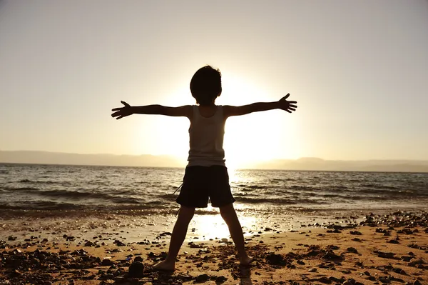 Silhouette di bambino sulla spiaggia, tenendo le mani in alto, verso il sole — Foto Stock