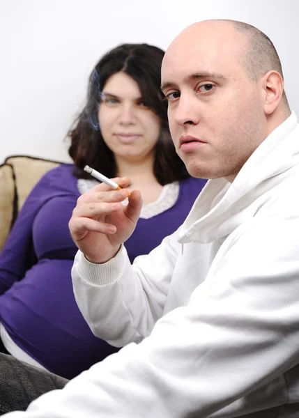 Мужчина курит рядом с беременной женщиной — стоковое фото