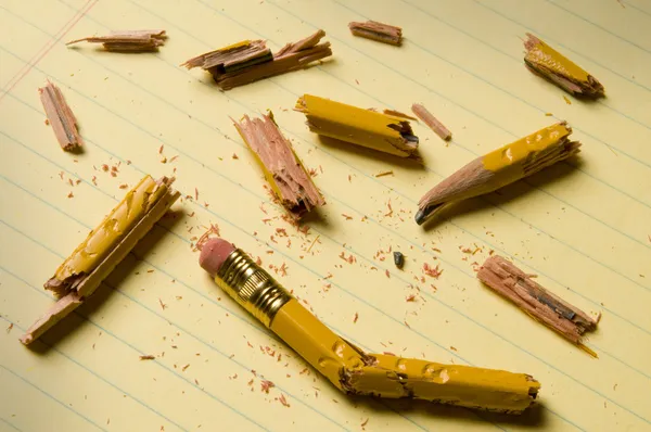 Broken pencil fragments on yellow paper — Stock Photo, Image