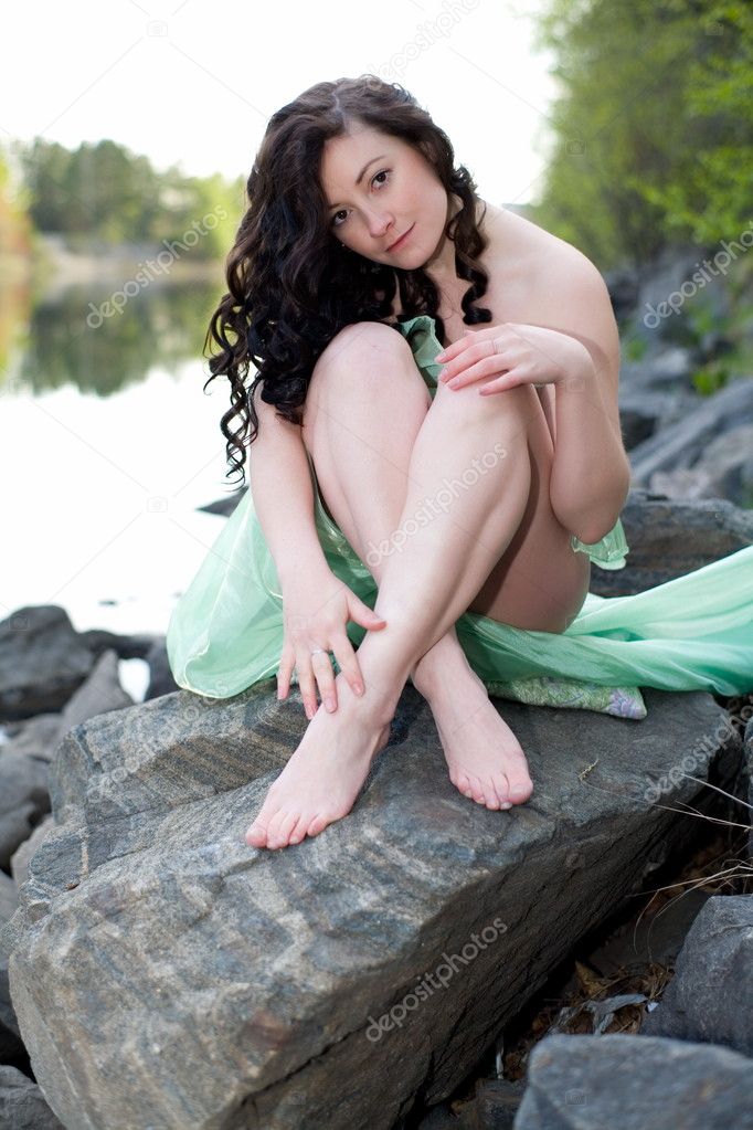 Young naked woman sitting on a wooden stump on forest background