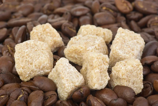 Poucos pedaços de açúcar mascavo sobre os grãos de café — Fotografia de Stock