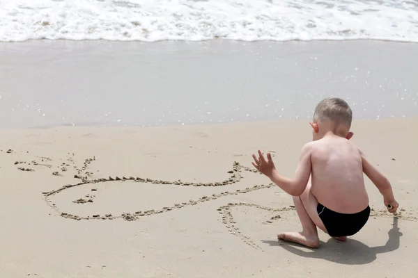Mały chłopiec rysuje ryb w piaszczystej plaży — Zdjęcie stockowe