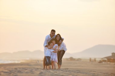 Mutlu genç aile gün batımında sahilde eğleniyor.