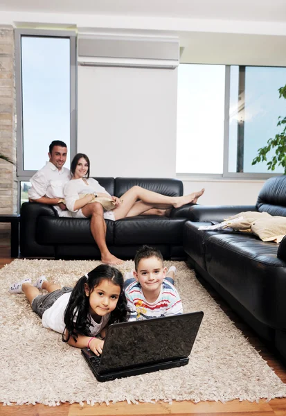 Счастливая молодая семья веселится и работает над ноутбуком дома — стоковое фото