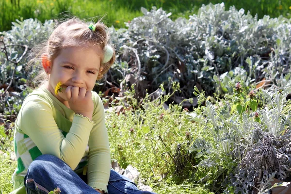 Маленькая девочка сидит в траве и думает: — стоковое фото