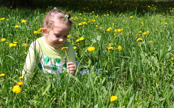 Маленька дівчинка сидить у траві і пахне кульбабою — стокове фото