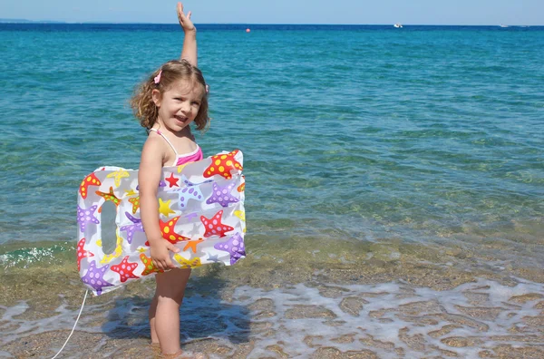 Happy little girl standing in the sea with hand up — Stock Photo, Image