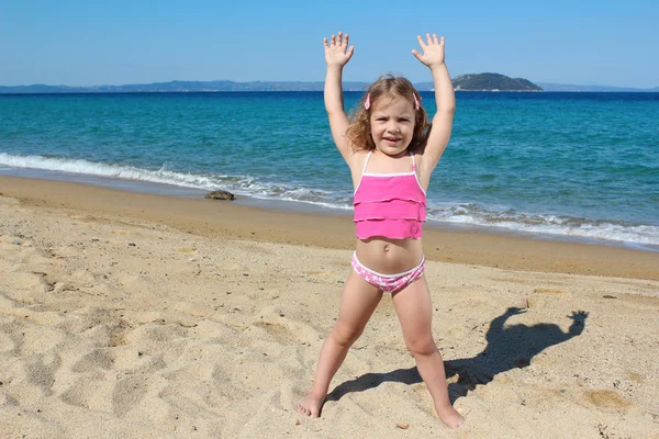 Little girl with hands up standing on the beach — Stock Photo, Image