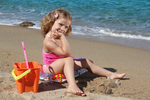Маленькая девочка с игрушками позирует на пляже — стоковое фото