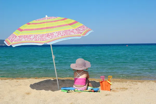 Little girl sitting on beach under sunshade — Stock Photo, Image