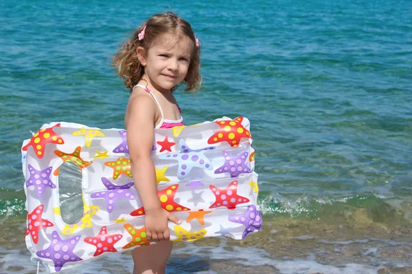 Маленькая девочка с воздушным ложем стоит в море — стоковое фото