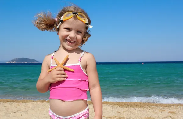 Bambina con stella marina in posa sulla spiaggia — Foto Stock