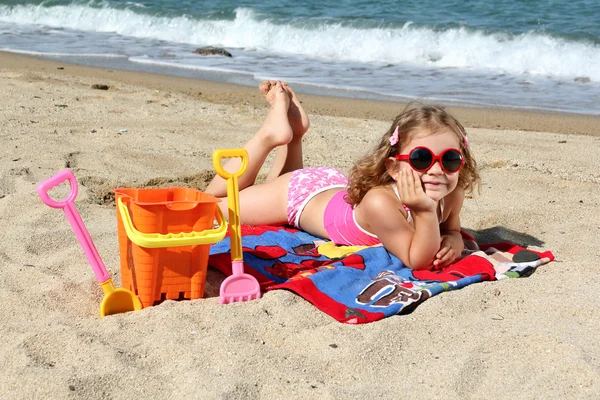 Little girl with sunglasses lying on the beach — Stock Photo, Image