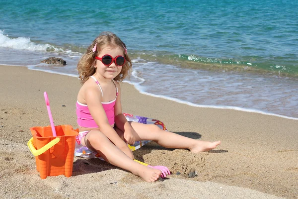 Kumsalda oynarken güneş gözlüklü küçük kız — Stok fotoğraf