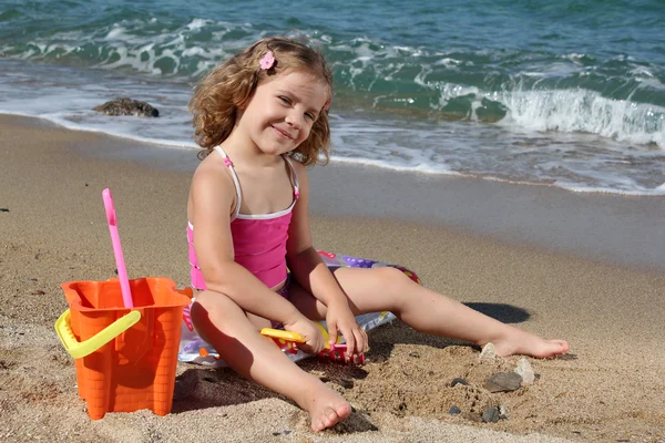 Küçük kız sahilde oturmuş ve oyuncaklar ile oynama — Stok fotoğraf