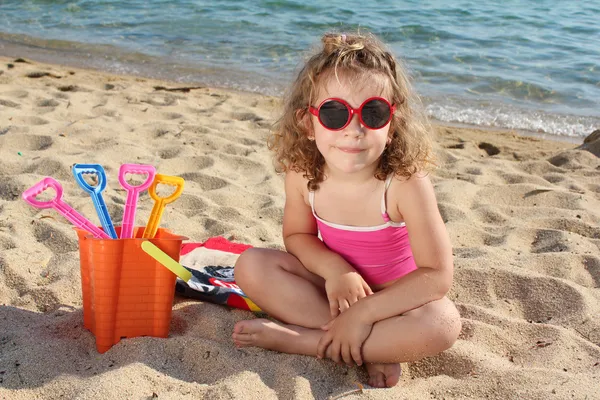 Little girl with sunglasses sitting on beach — Stock Photo, Image