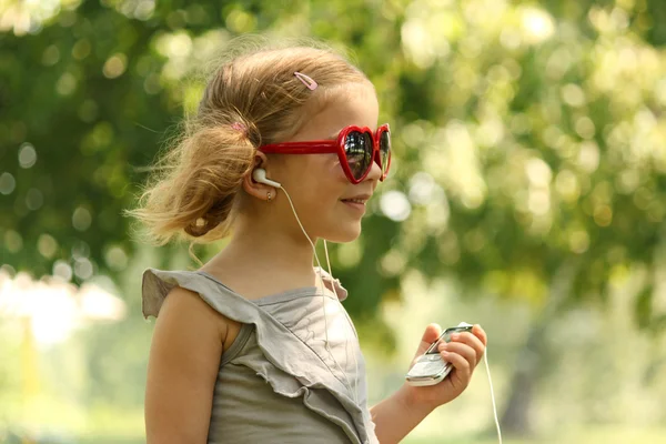 Skönhet lilla flicka lyssnar musik i parken — Stockfoto