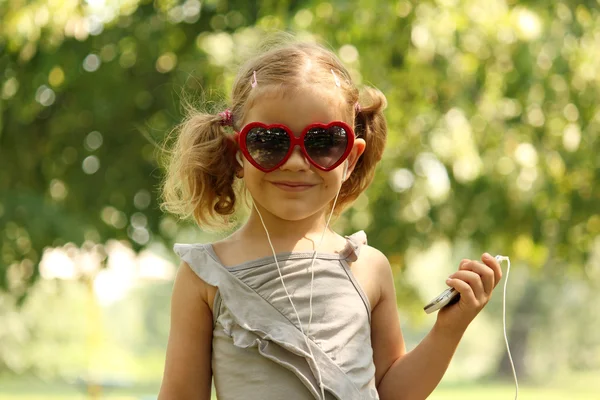 Маленькая девочка в солнечных очках слушает музыку — стоковое фото