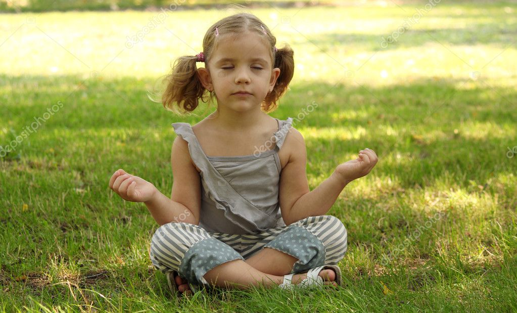 Little cute baby girl doing yoga exercise on the grass at beautiful sun  light in green summer park. Stock Photo