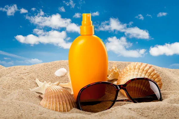 Suntan oil and dark glasses on the beach — Stock Photo, Image