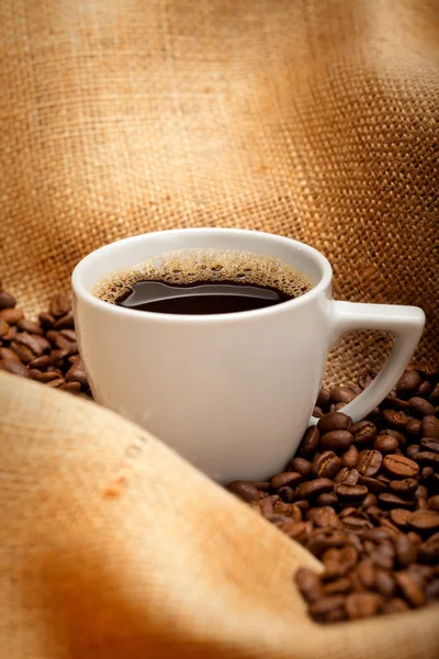 Filiżanka kawy i fasoli na tle juty — Zdjęcie stockowe