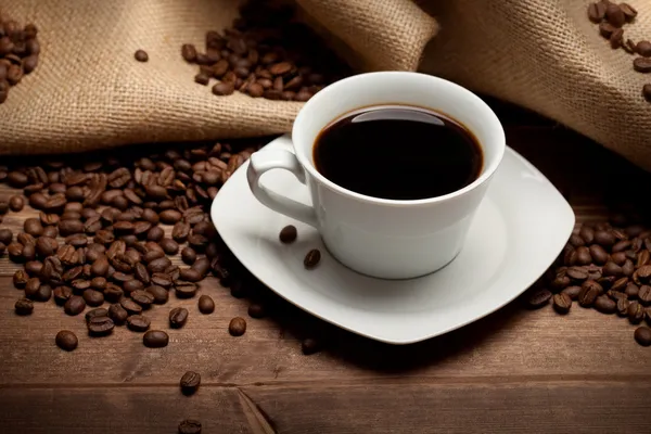 Tasse Kaffee und Bohnen auf Jute-Hintergrund — Stockfoto