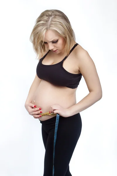 Pregnant woman measuring her waistline with tape — Stock Photo, Image