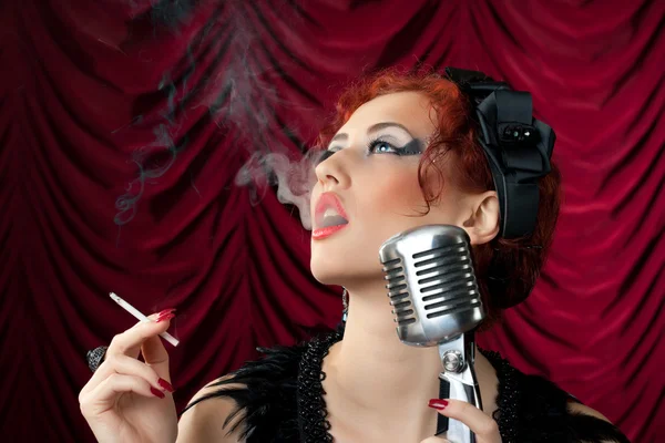Hermosa pelirroja fumando cigarrillo cerca de micrófono vintage — Foto de Stock