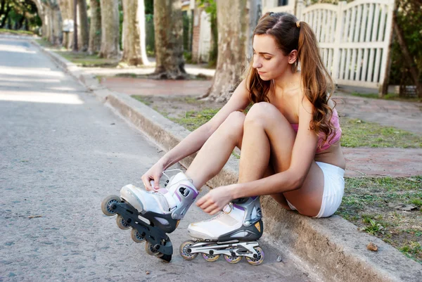 Ein hübsches Mädchen bindet die Schnürsenkel auf ihren Rollerblades — Stockfoto