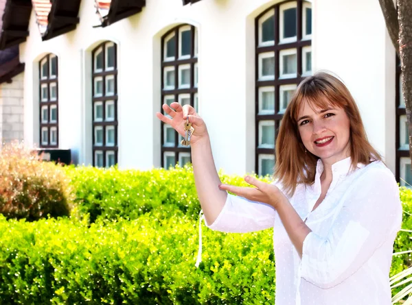 De vrouw met sleutels in een hand tegen het huis is jong — Stockfoto