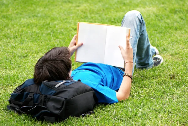 Парень лежит на траве и читает книгу — стоковое фото