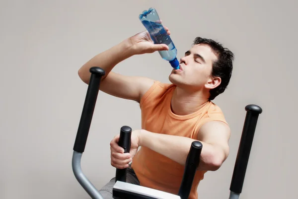 Boy on training apparatus drinks water in sportclub — Stock Photo, Image
