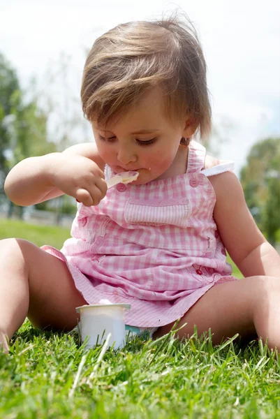 Holčička jí jogurt sedí trávě — Stock fotografie