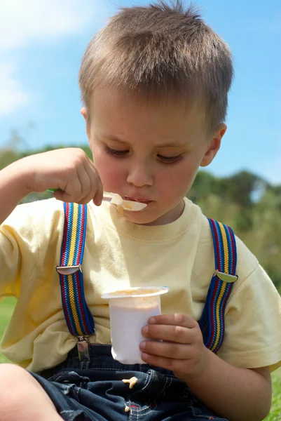 El niño es apetitoso come yogur sentado en una hierba en — Foto de Stock
