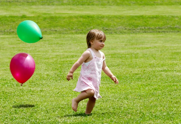 Het kleine meisje wordt uitgevoerd op een gras met ballonnen — Stockfoto