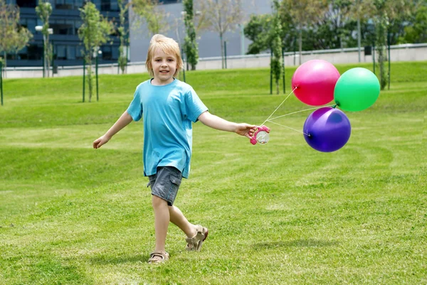 Маленький хлопчик біжить на траві з повітряними кульками — стокове фото