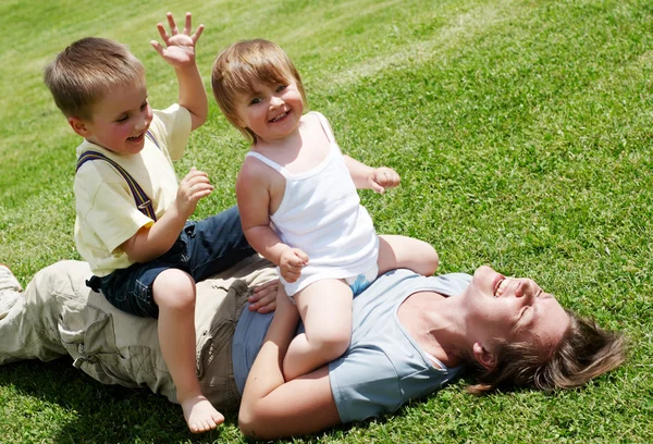 Glückliche Mutter spielt mit Kindern auf dem Rasen — Stockfoto