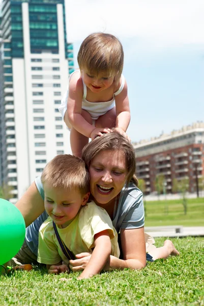 Счастливая мать играет с детьми на лужайке — стоковое фото