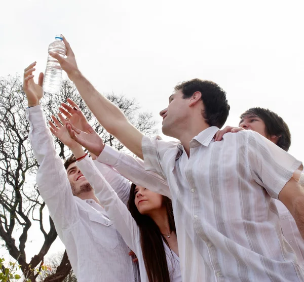 Group of young men stretching hands to a bottle with water — Stock Photo, Image