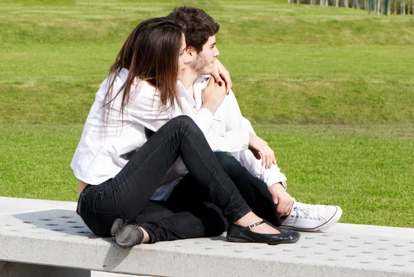 Jonge liefde in park op een bankje — Stockfoto