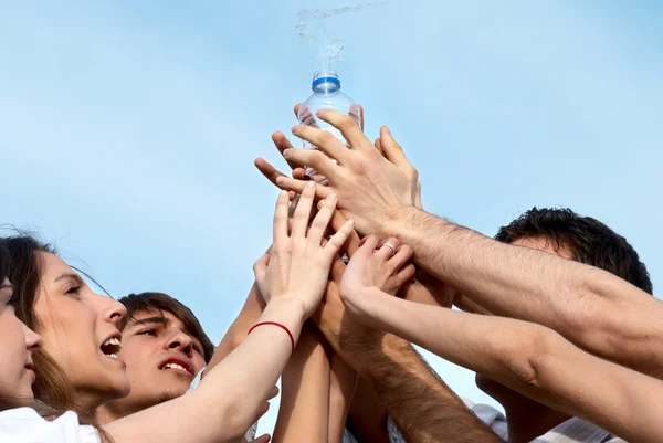 Groupe de jeunes hommes étendant les mains à une bouteille d'eau — Photo